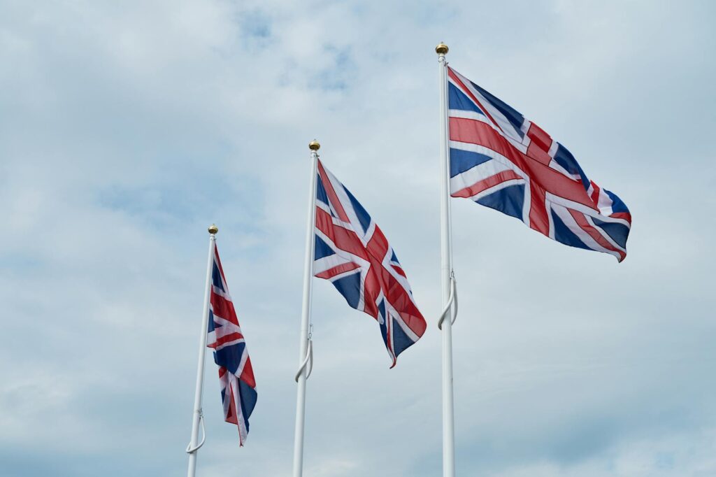 uk Immigration Reforms — Three Union Jack flags waving against a cloudy sky in Penrith, England.